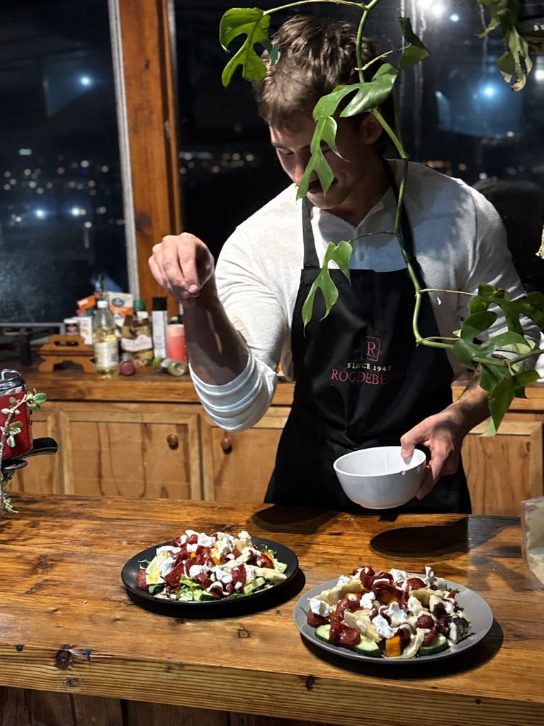 Matthew seasoning two plated salads at a wooden counter