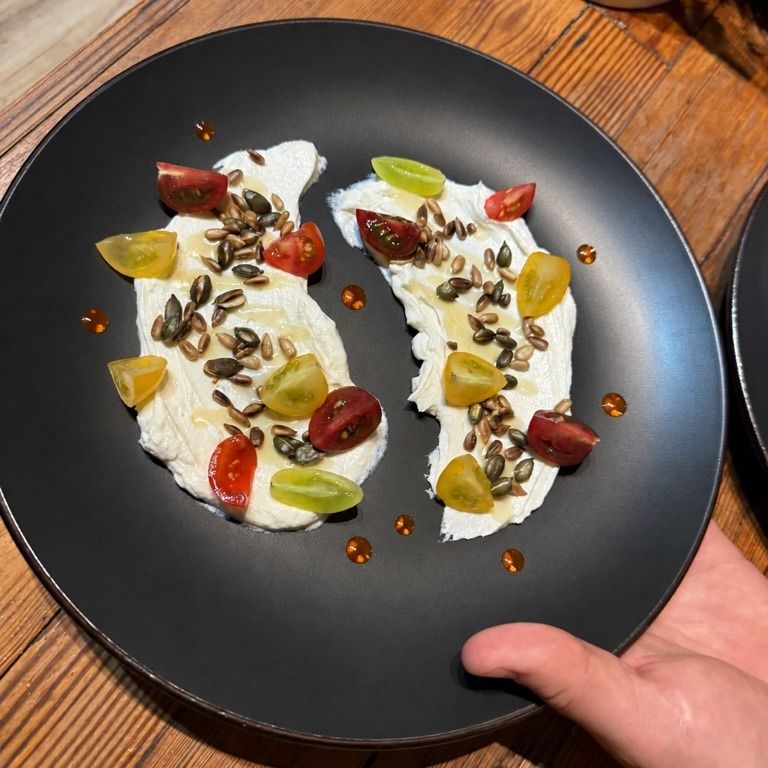 Whipped cheese on a charcoal plate with heirloom tomatoes and toasted seeds